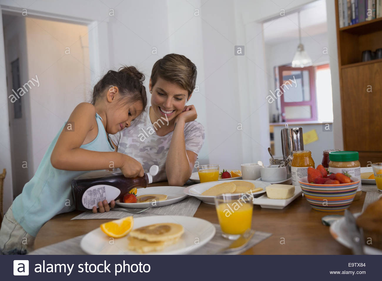Mother watching daughter pour syrup on pancakes Stock Photo