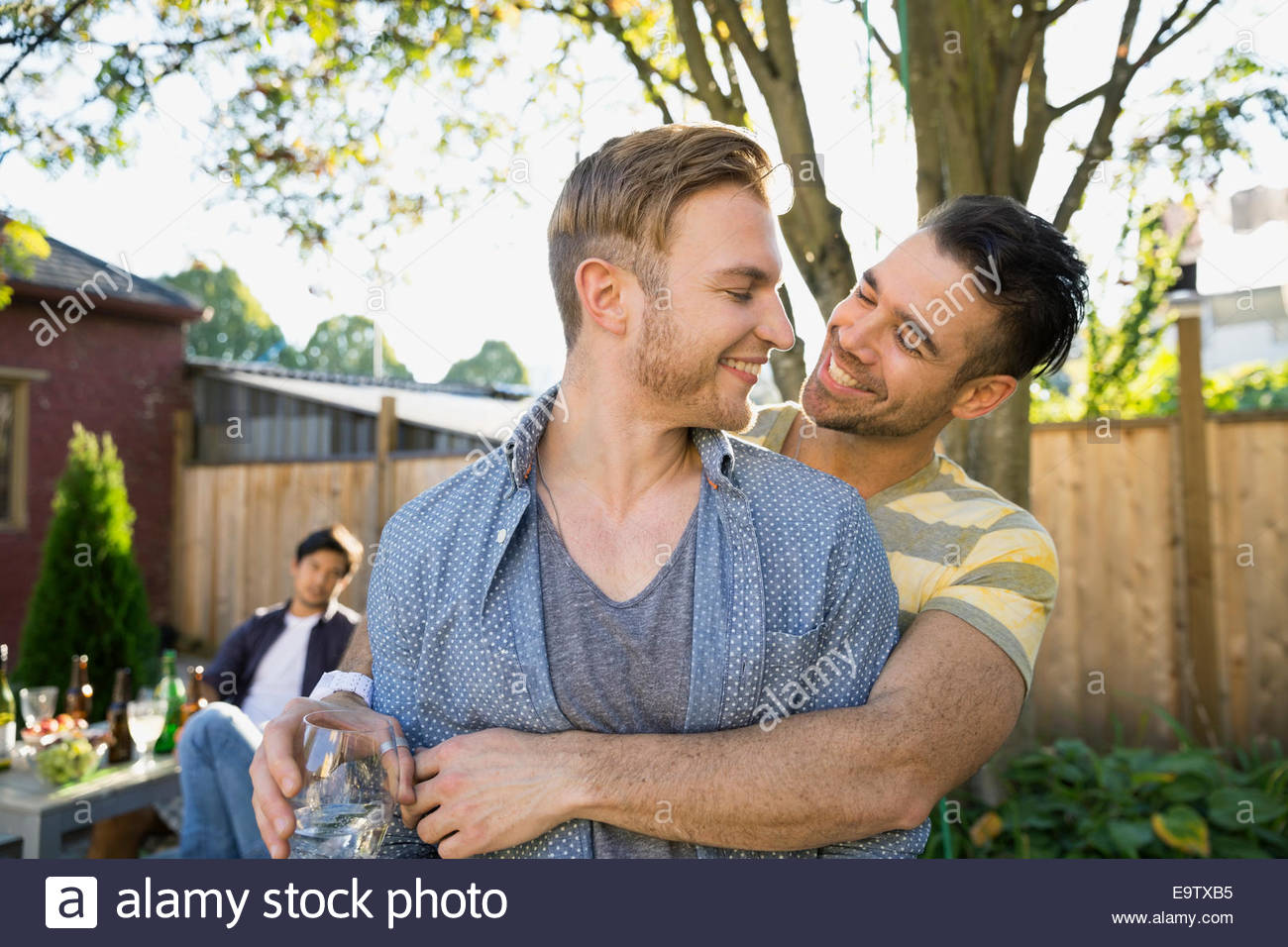 Homosexual couple hugging at backyard barbecue Stock Photo