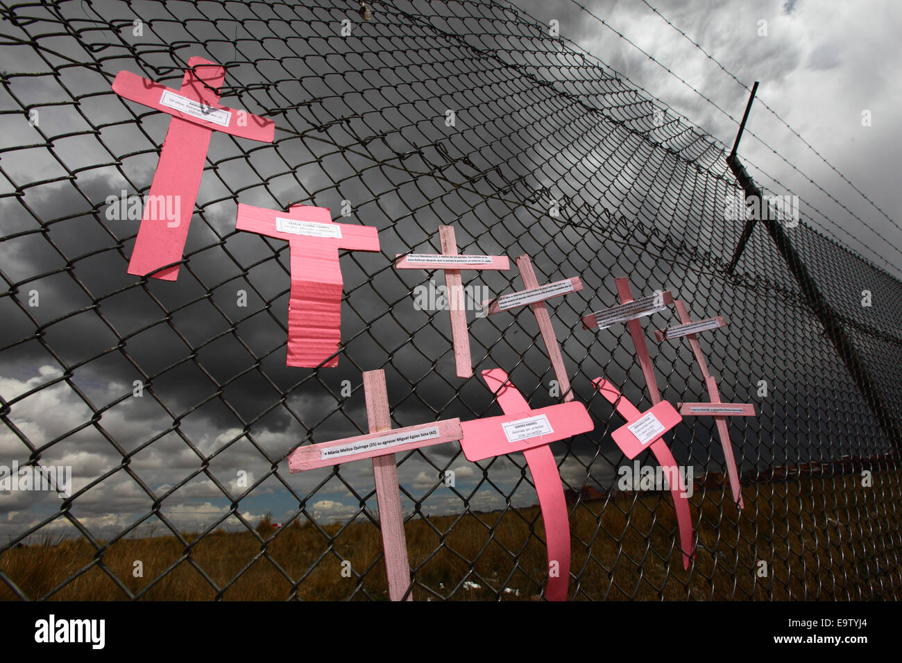 EL ALTO, BOLIVIA, 2nd November 2014. Crosses with the names of women against dark skies on a wire mesh fence, part of a memorial for recent victims of femicide and domestic violence against women. According to a WHO report in January 2013 Bolivia is the country with the highest rate of violence against women in Latin America. Credit:  James Brunker / Alamy Live News Stock Photo