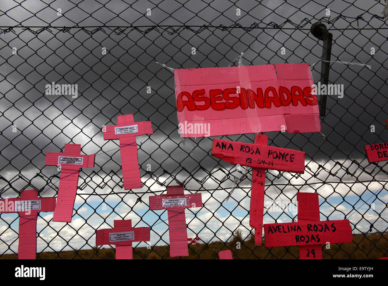 EL ALTO, BOLIVIA, 2nd November 2014. Crosses with the names of women against dark skies on a wire mesh fence, part of a memorial for recent victims of femicide and domestic violence against women. According to a WHO report in January 2013 Bolivia is the country with the highest rate of violence against women in Latin America. Credit:  James Brunker / Alamy Live News Stock Photo