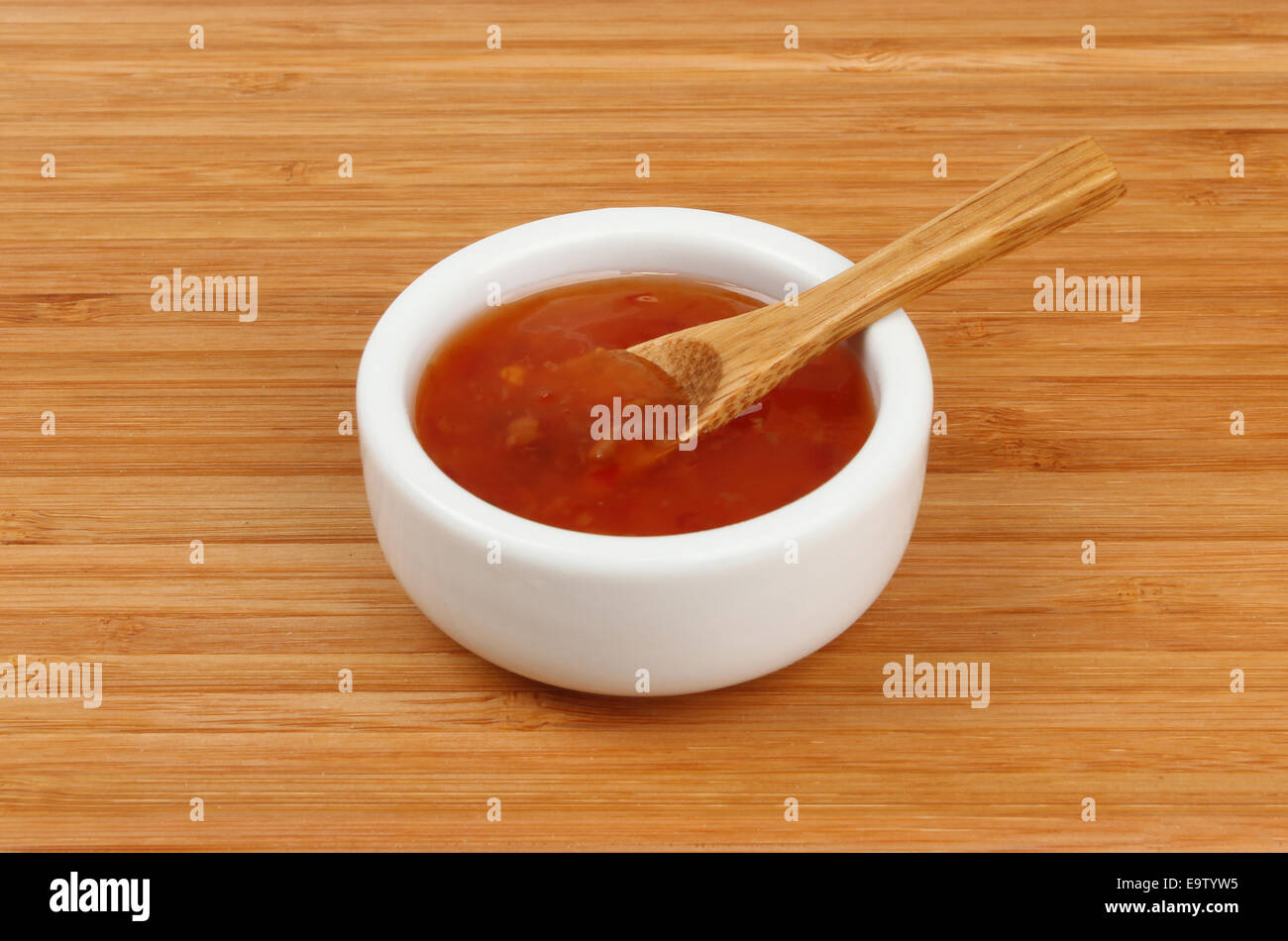 Sweet chilli dipping sauce in a ramekin with a spoon on a bamboo board Stock Photo