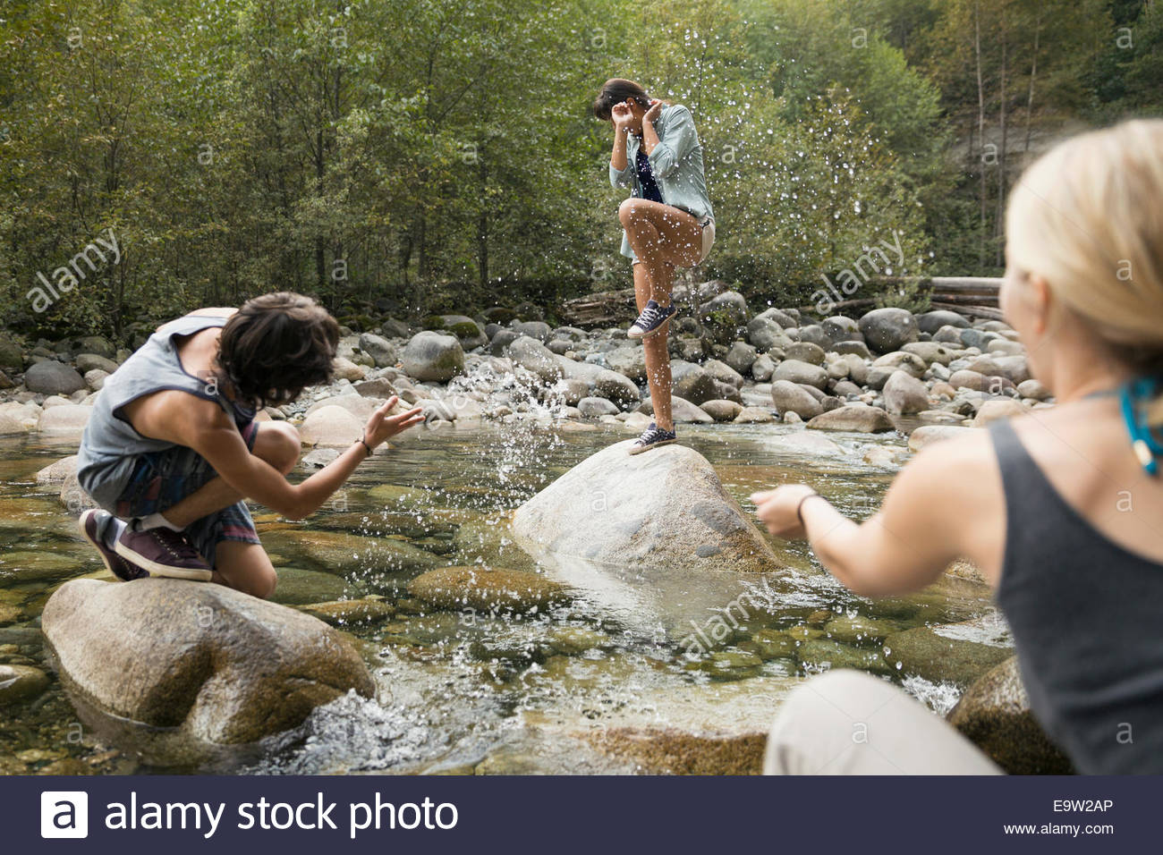 Friends splashing woman on rock over creek Stock Photo