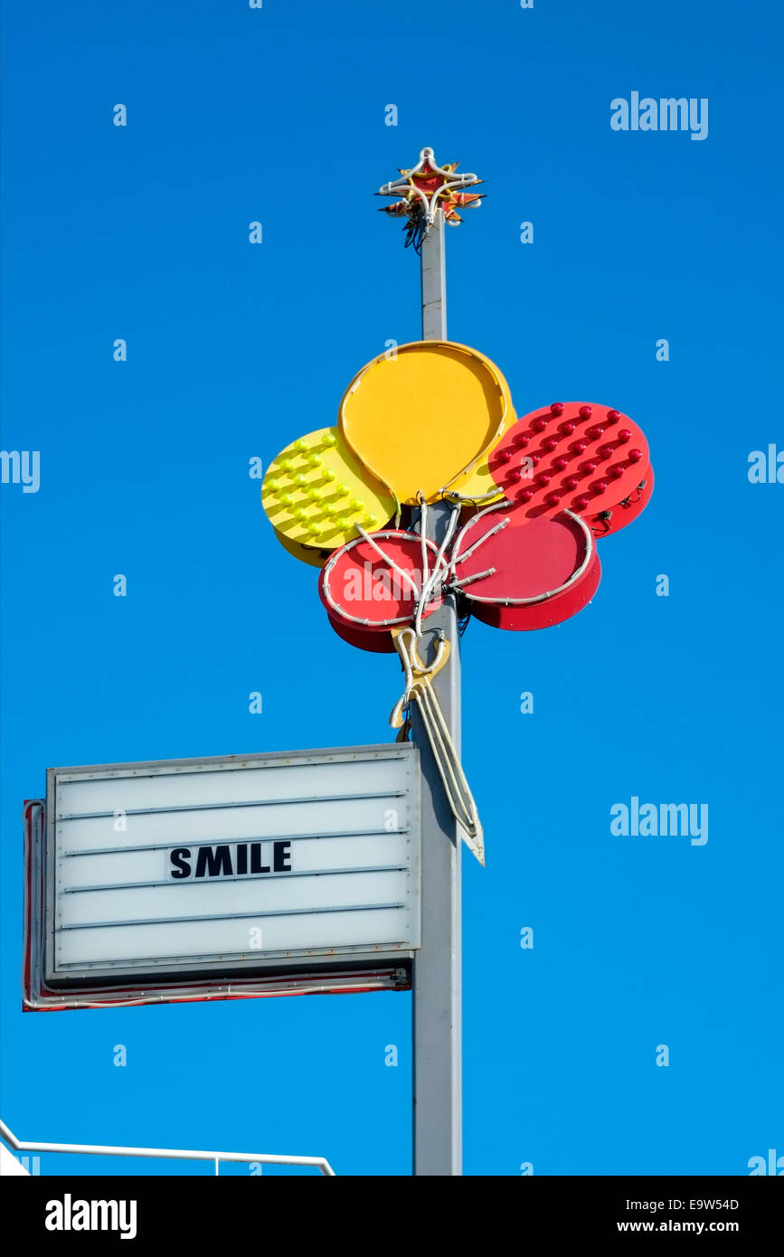 colourful neon sign depicting red and yellow balloons with the word smile against a deep blue sky england uk Stock Photo