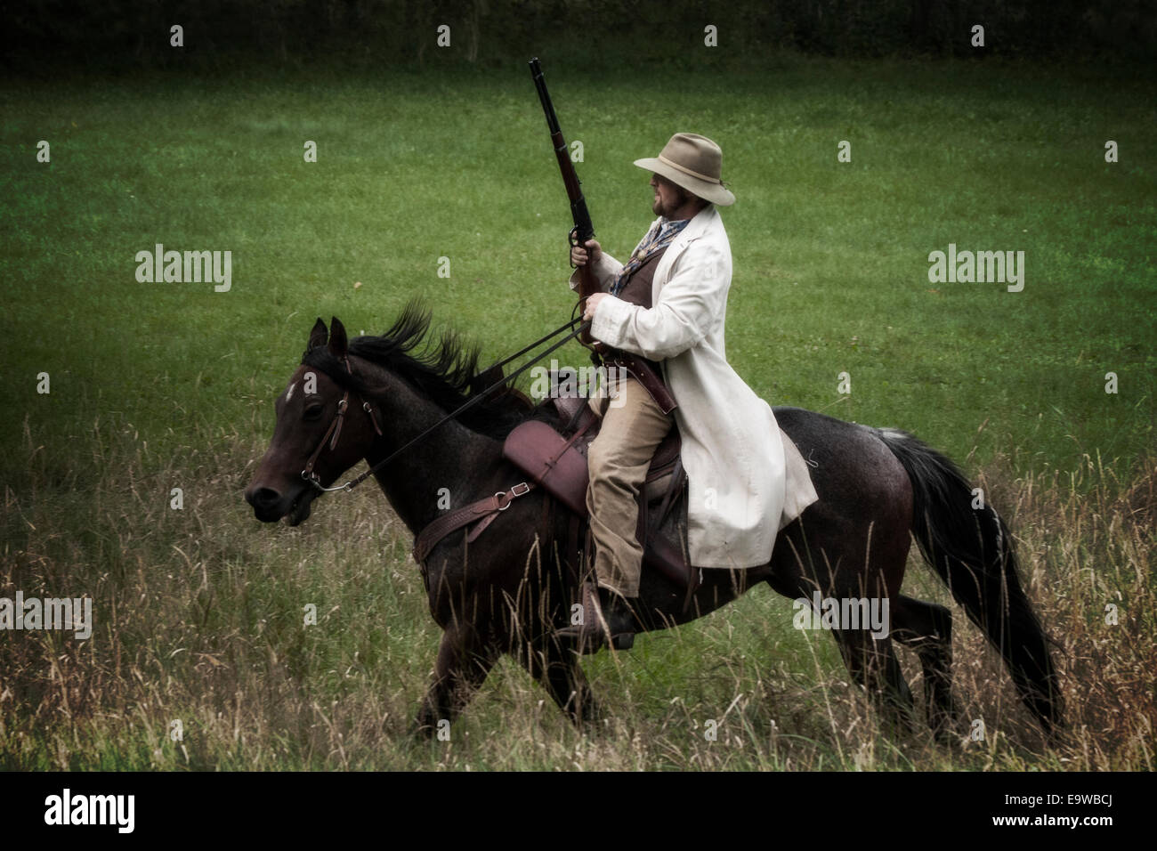 cowboy riding countryside country western old west man male rider horse rifle gun retro vintage past history historical field ho Stock Photo