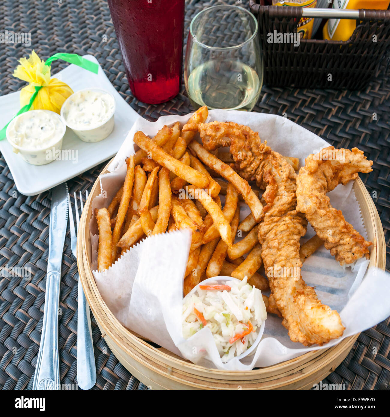 Fish and chips basket with battered flounder, crispy, seasoned french fries, cole slaw, tartar sauce and a glass of white wine. Stock Photo