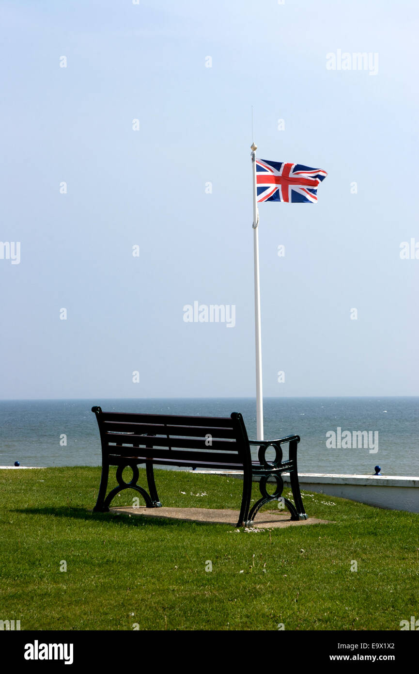 Seaside bench and British flag overlooking sea on a windy and sunny day Stock Photo