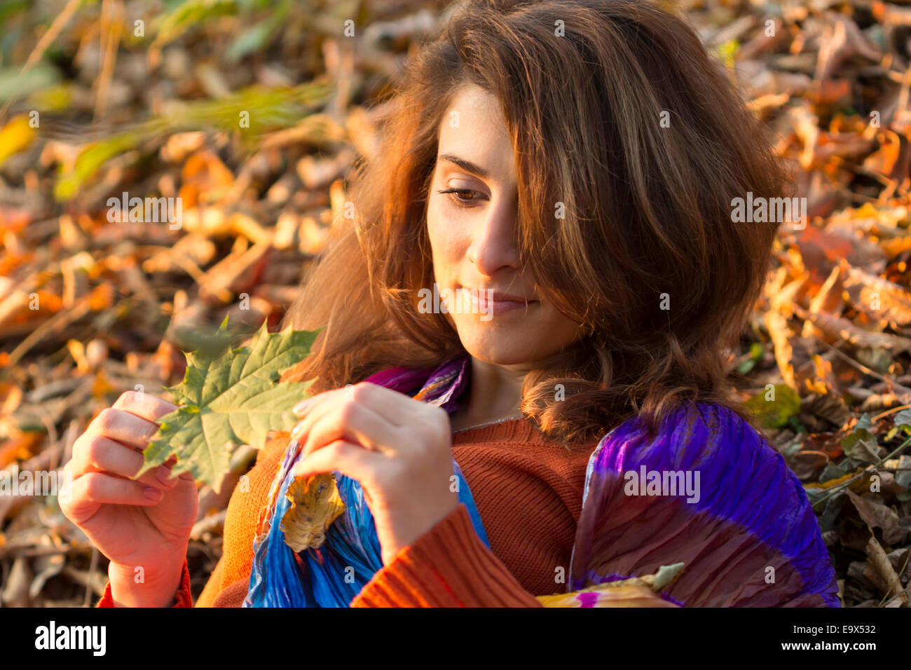 Portrait of young woman in autumn season looking to a leaf, outdoor shot Stock Photo