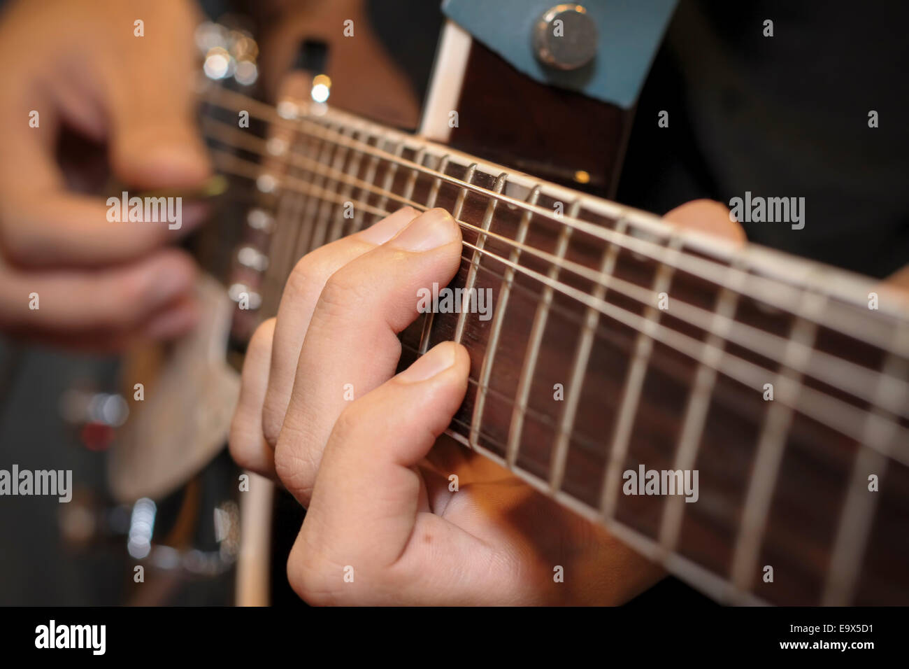 close up shot of a man with his fingers on the frets of a guitar playing Stock Photo