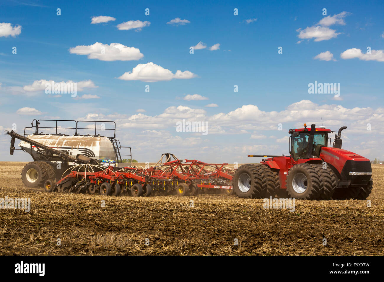 Tractor seeding field with clouds and blue sky; Alberta, Canada Stock