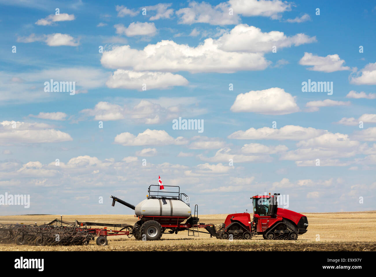 Tractor seeding field with clouds and blue sky; Alberta, Canada Stock