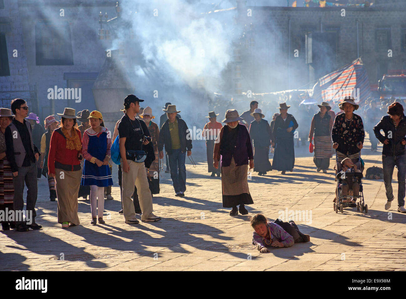 [Editorial Use Only] Tibetans walking the Barkhor in Lhasa, Tibet, while a pilgrim repeatedly prostrate herself on the ground Stock Photo