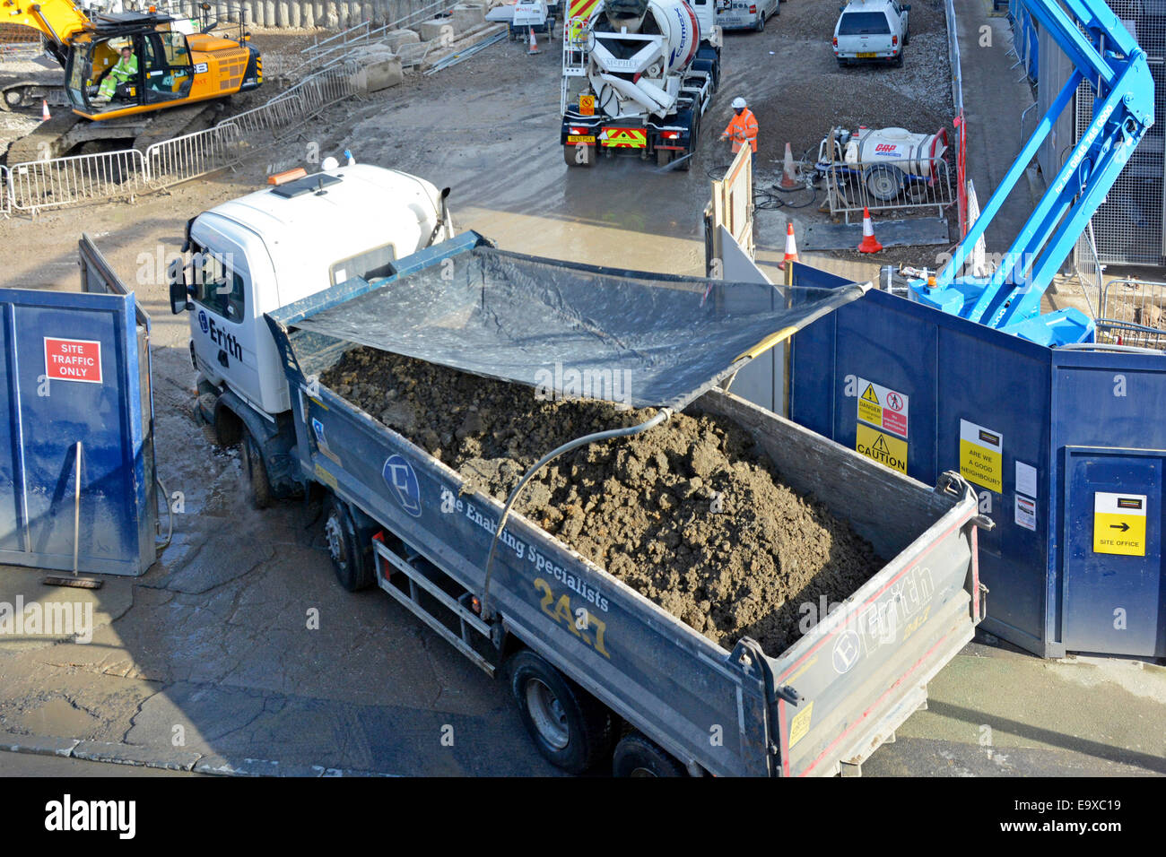 Tipper truck driver using mirrors reversing from building site dust net covering & locating over excavated earth (banksman out of shot)  Southwark UK Stock Photo