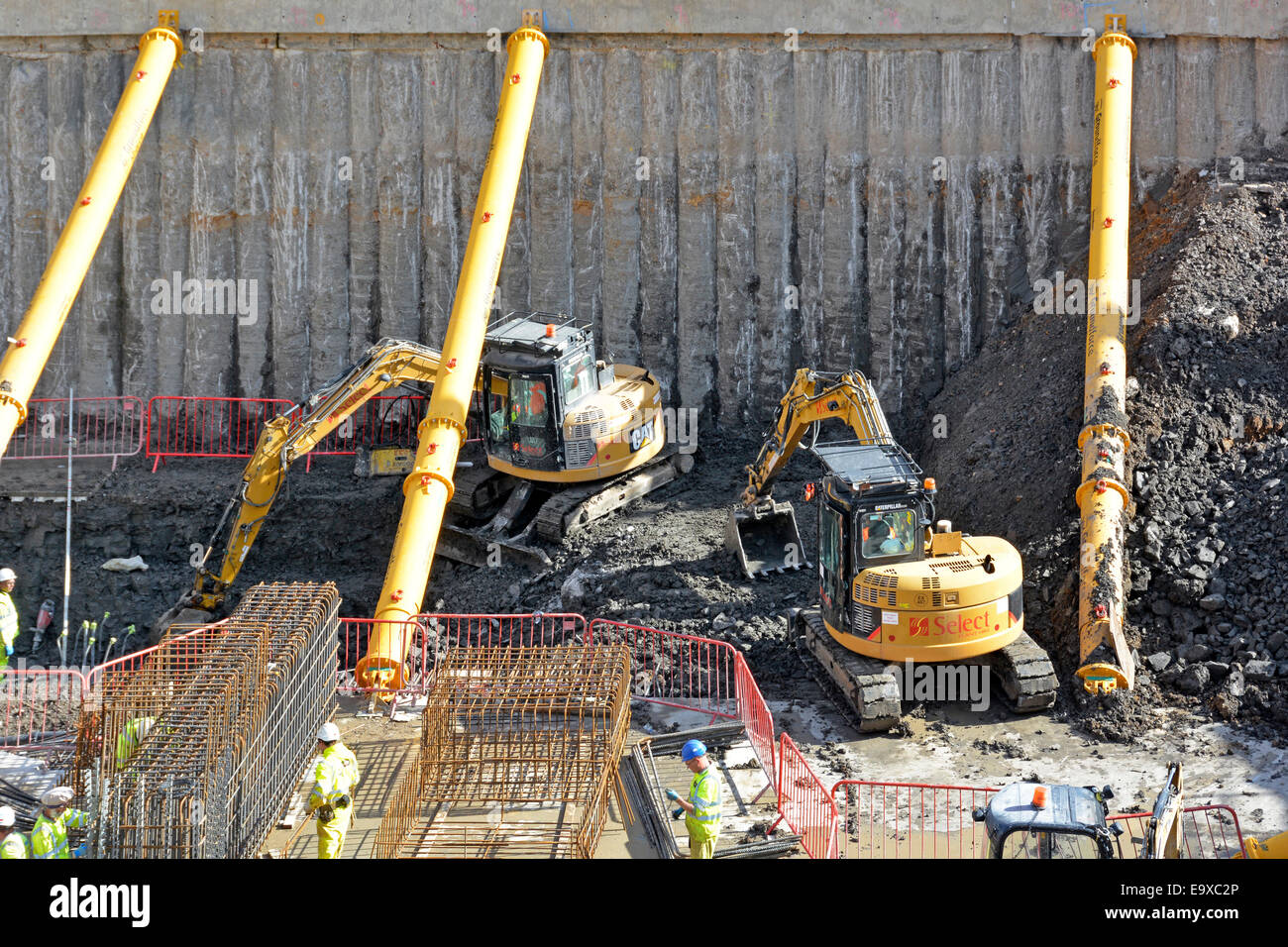 Construction building site work between hydraulic tubular shoring struts Cat excavator diggers expose concrete piled basement retaining wall London UK Stock Photo