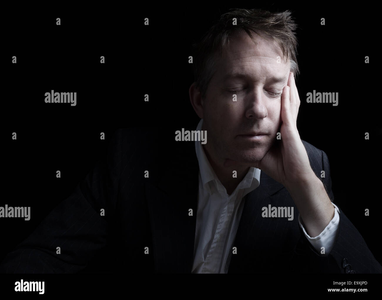 Portrait of businessman closing eyes while working late at night on black background with copy space Stock Photo