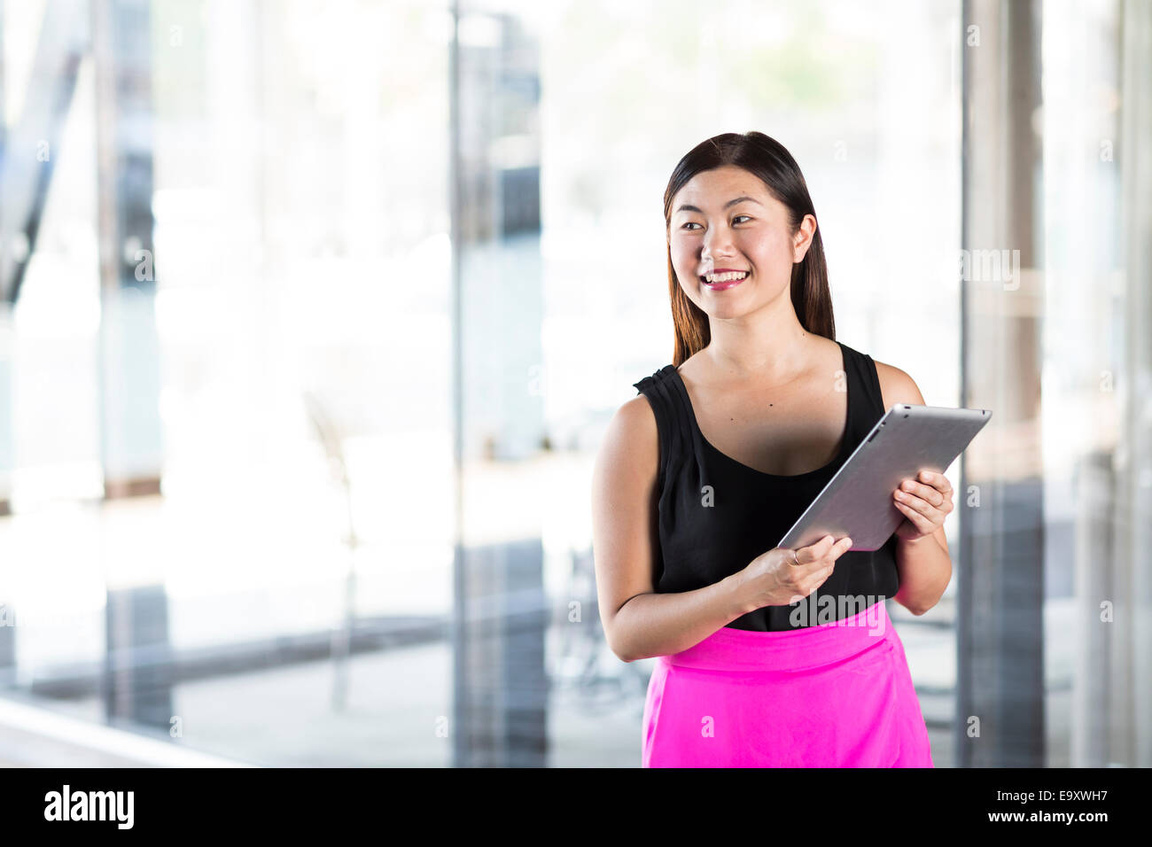 A young Asian woman using her tablet whilst she is out and about in an ...