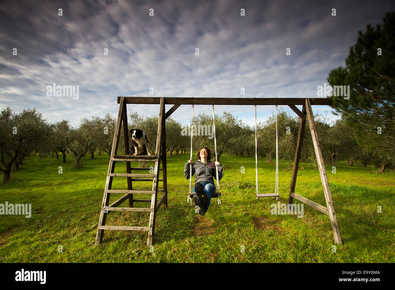 Girl swinging on a wooden swing in front of an olive grove, Tuscany, Italy Stock Photo