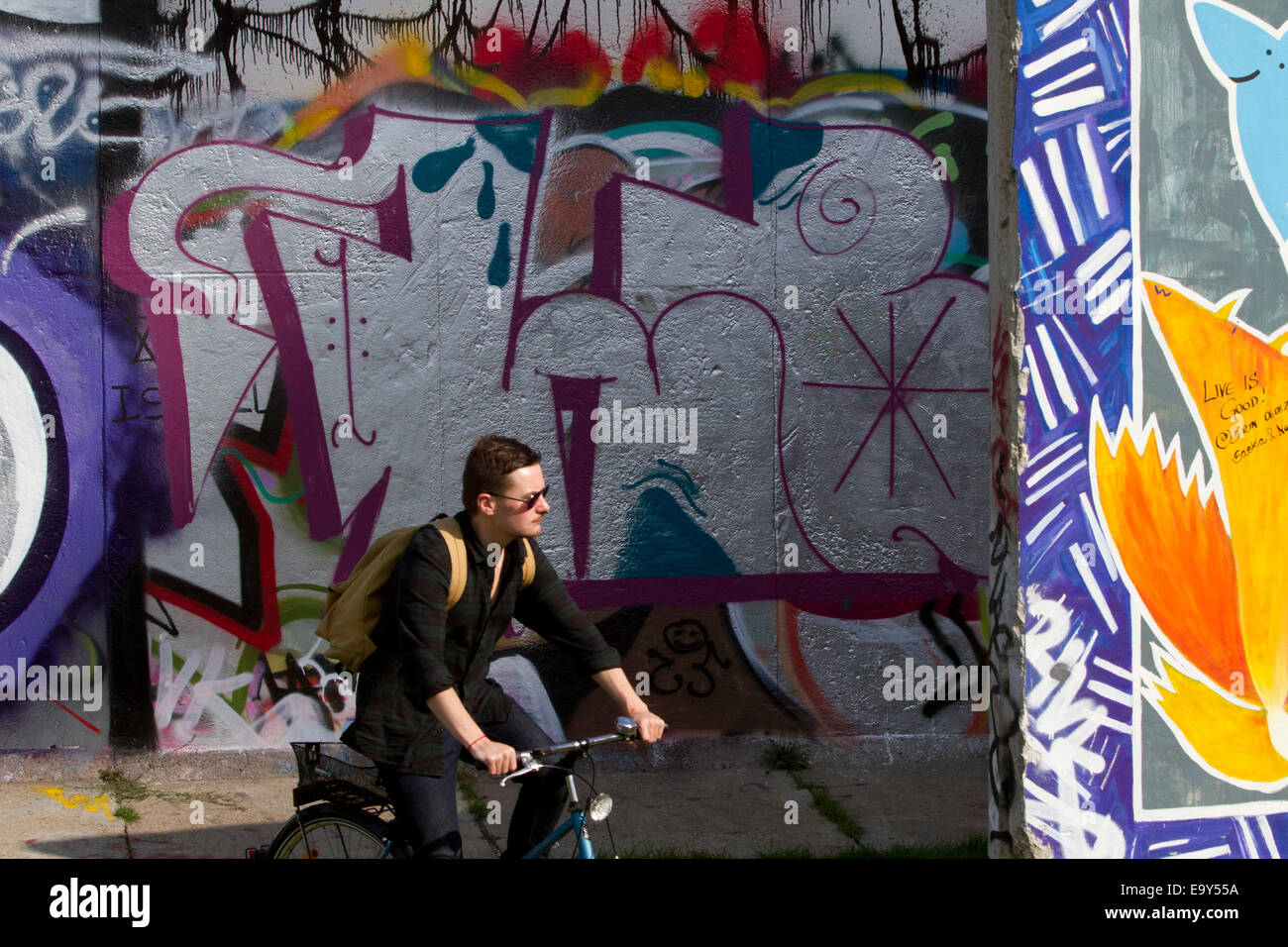 Man on bicycle Berlin wall graffiti sunny colouful Stock Photo