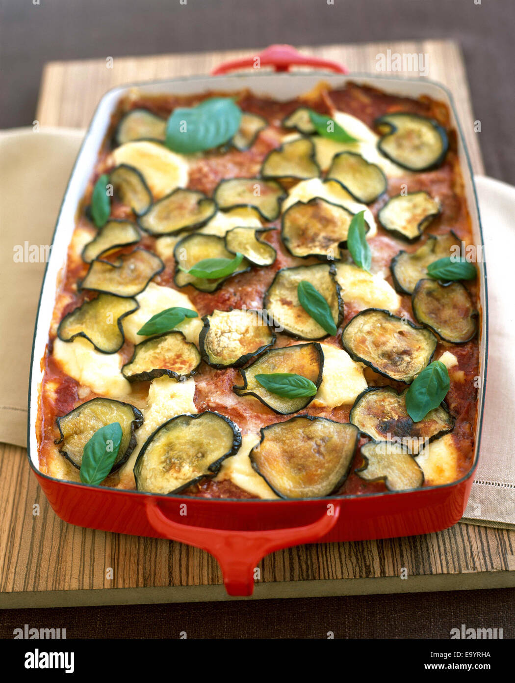 baked lasagna in red pan with eggplant slices and basil leaves Stock Photo