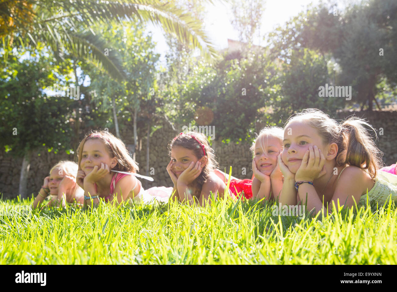 Five girls lying in a row in garden with chins on hands Stock Photo
