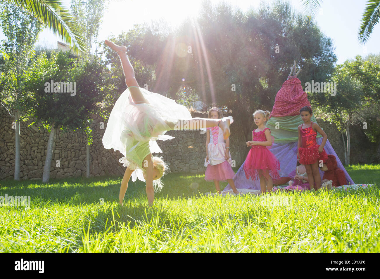 Girls watching friend in fairy costume doing cartwheel in garden Stock Photo