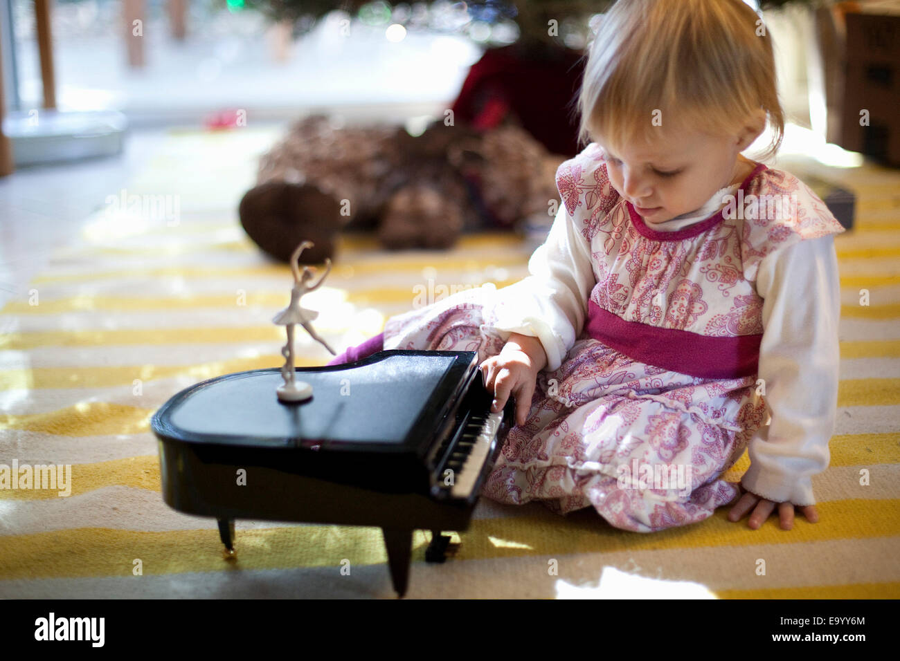 Female Toddler Sitting On Living Room Floor Playing With Toy Piano