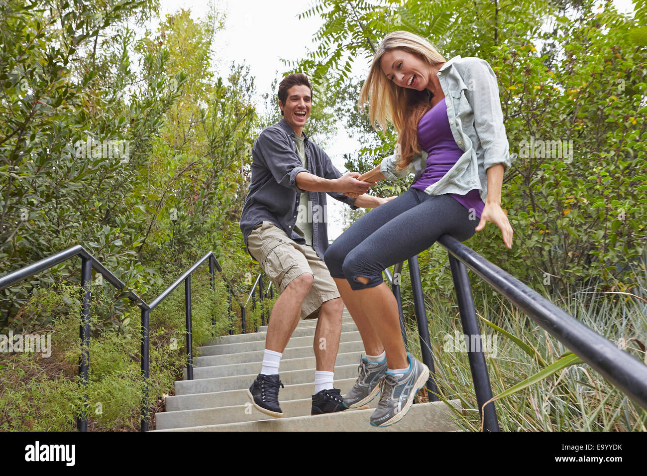 Couple sliding down step railing in forest Stock Photo