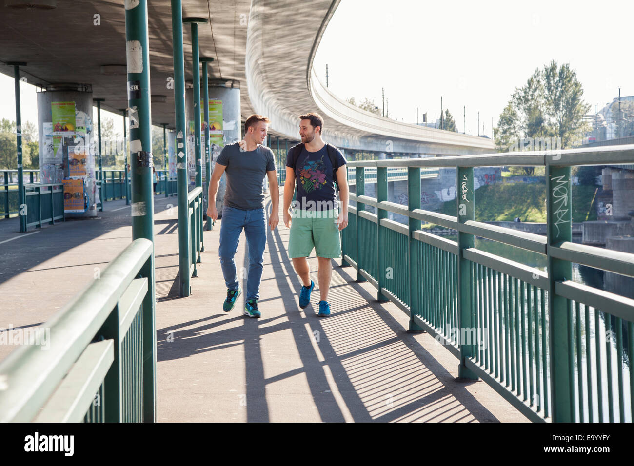Two young men chatting as they walk over bridge Stock Photo