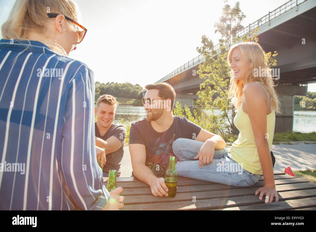 Four young friends drinking beer on riverside picnic bench Stock Photo