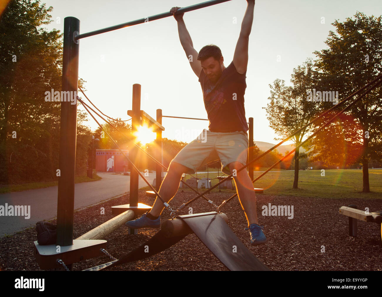 Silhouetted young man swinging on playground climbing frame at sunset Stock Photo