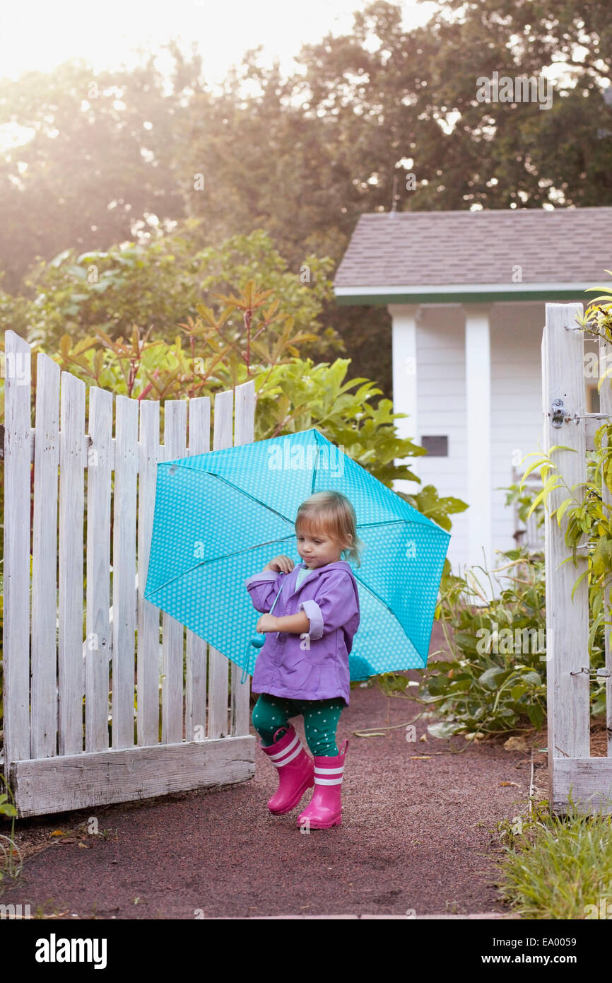 Female toddler walking in garden carrying umbrella Stock Photo