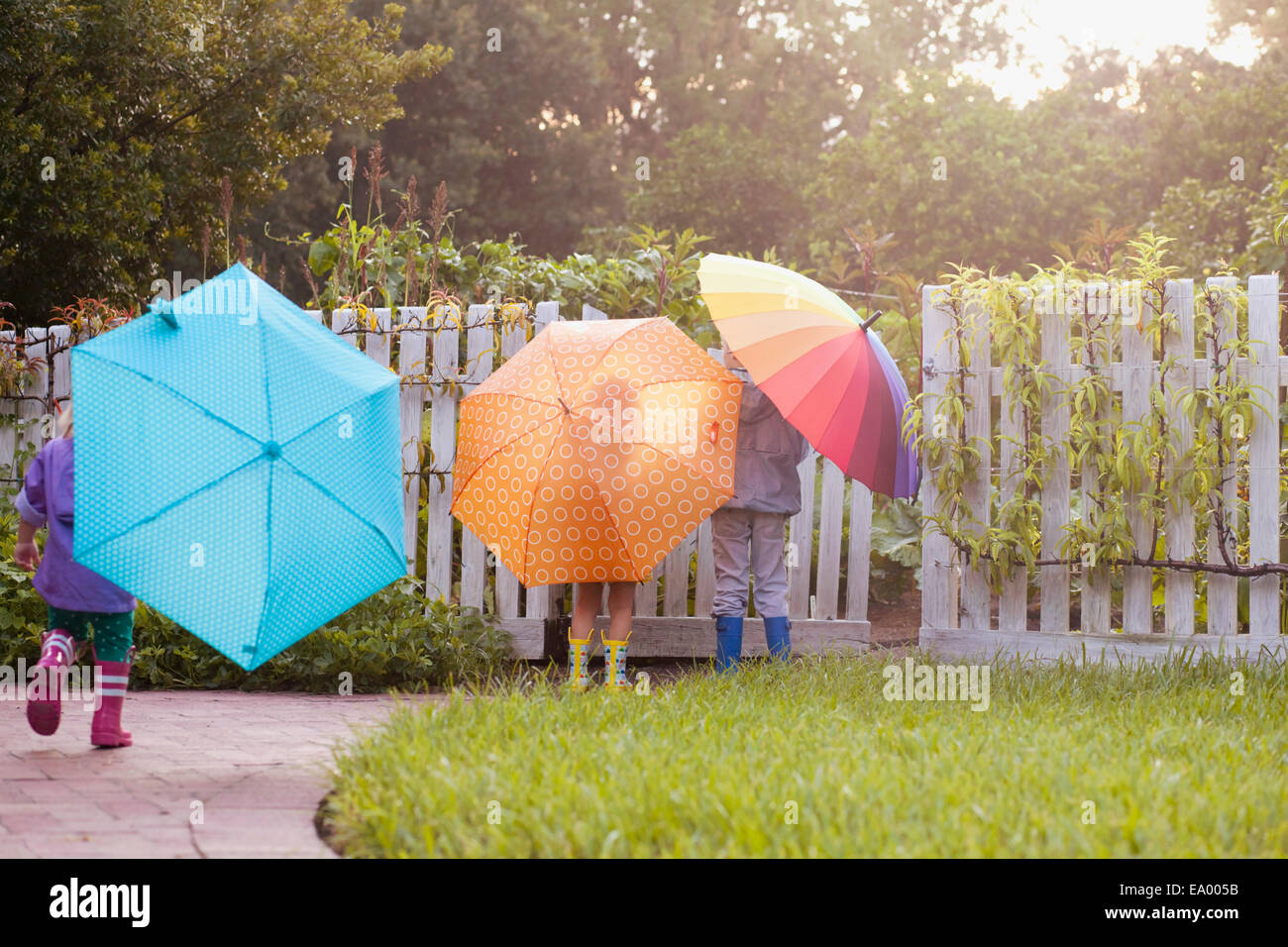Boy and two sisters playing in garden carrying umbrellas Stock Photo