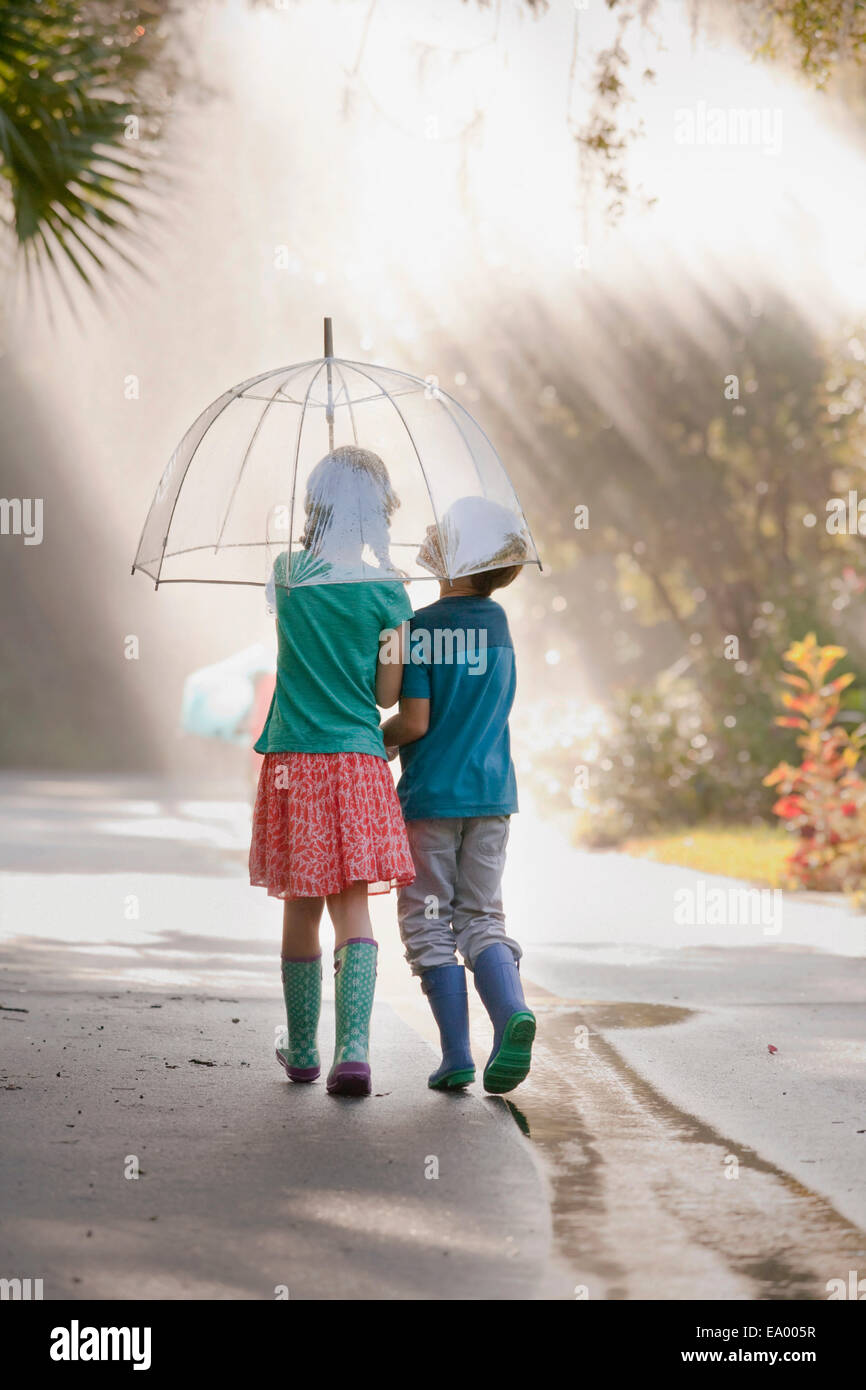 Rear view of boy and girl carrying umbrella on street Stock Photo