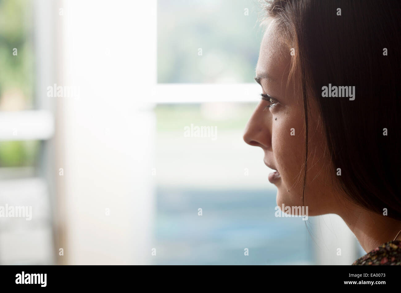 Close up portrait of young woman gazing out of window Stock Photo