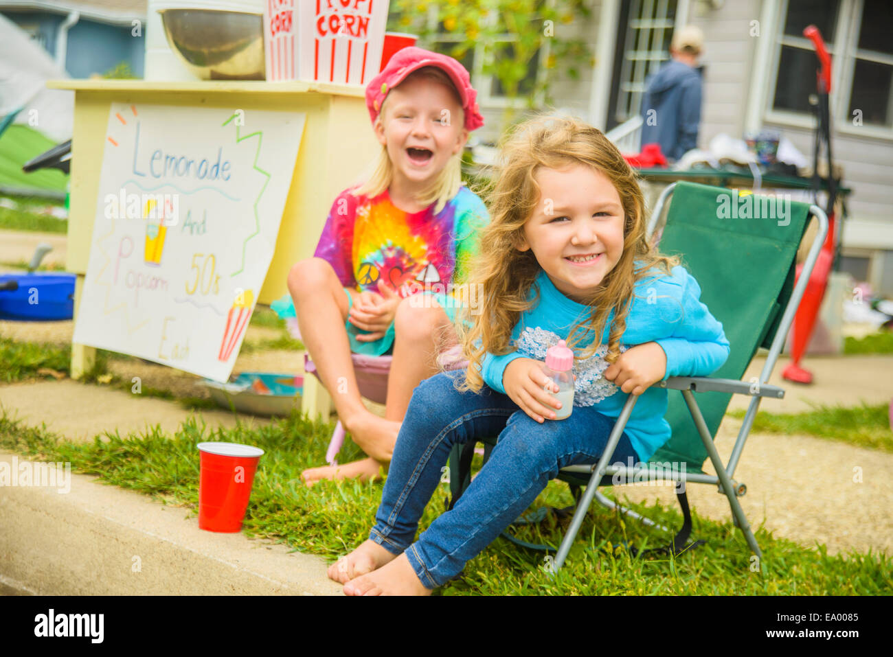 Candid portrait of two smiling girls selling lemonade and popcorn at yard sale Stock Photo