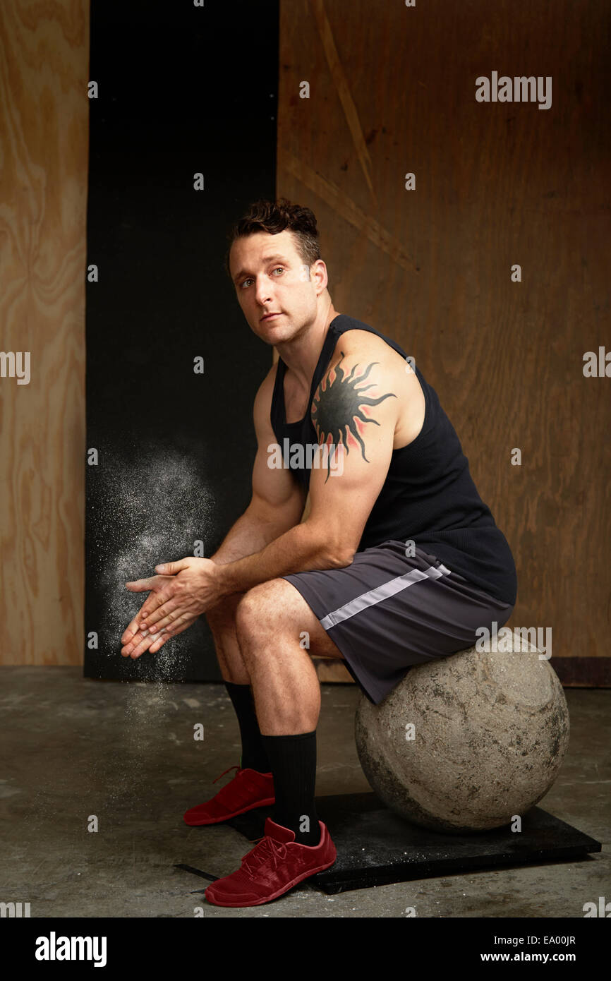 Portrait of mid adult man sitting on atlas ball in gym Stock Photo