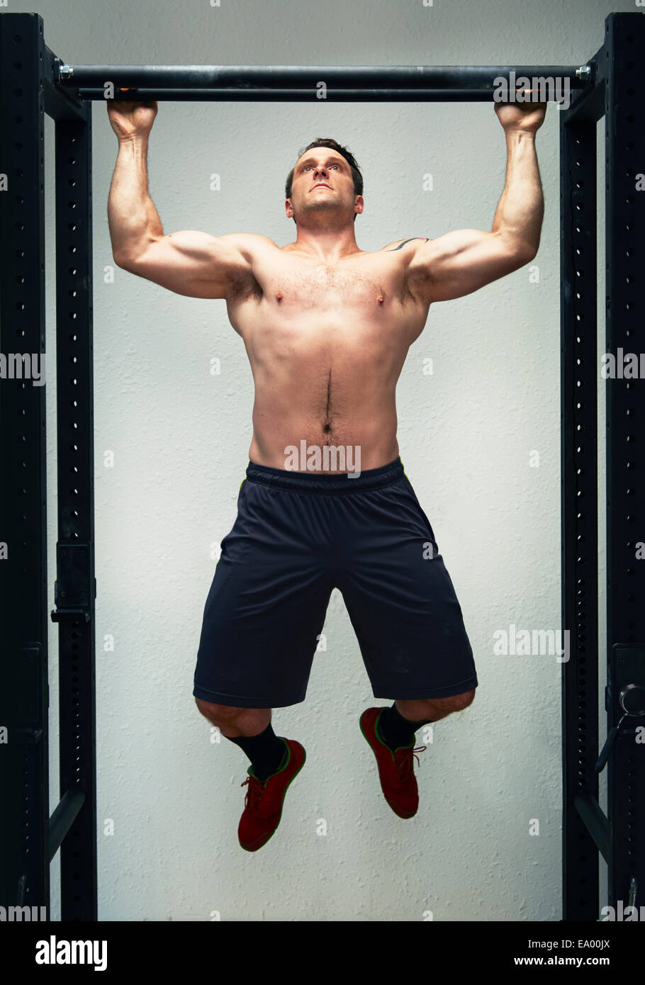 Mid adult male doing pull ups on exercise bar in gym Stock Photo