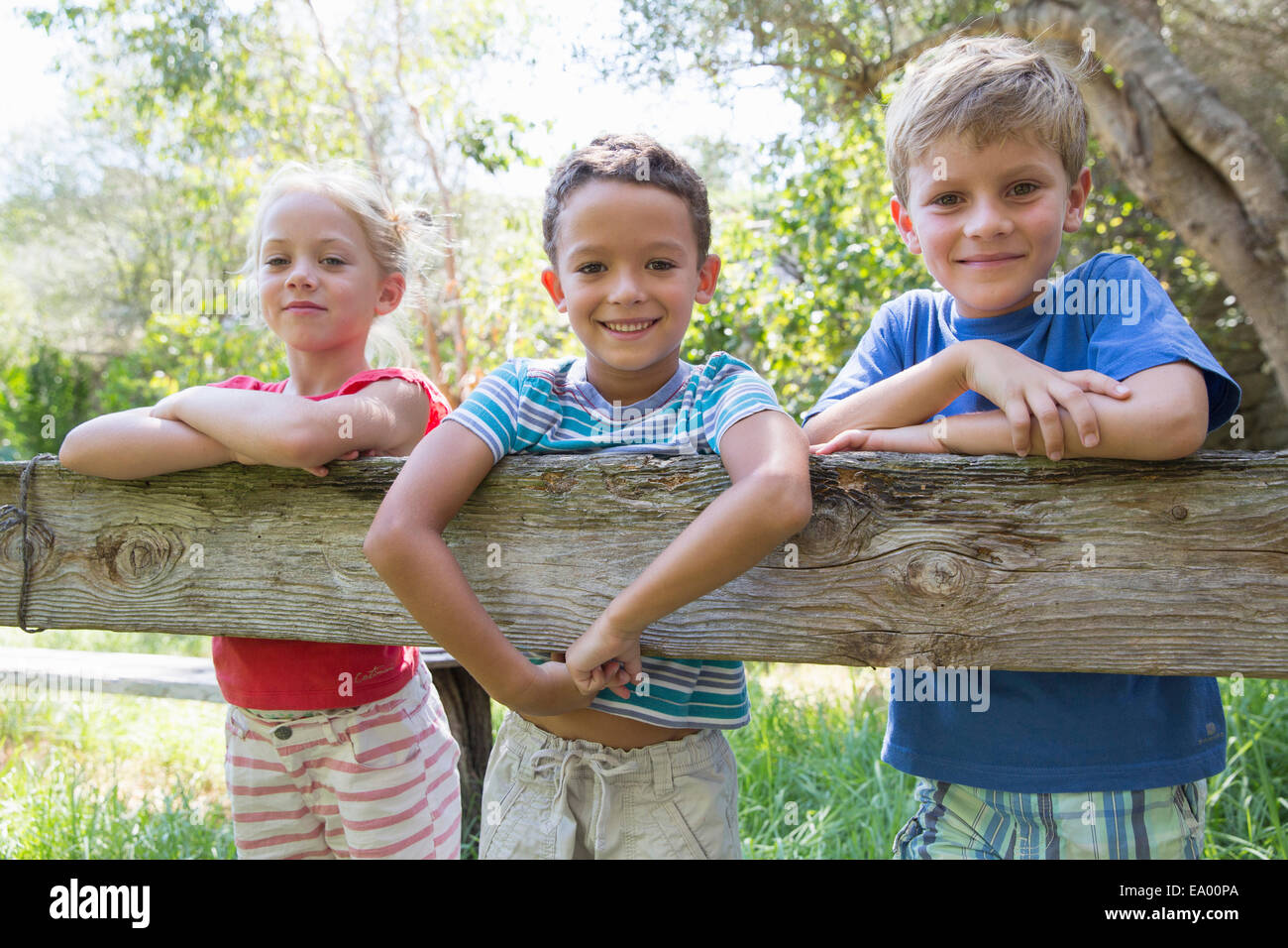 Three children in leaning over garden fence Stock Photo