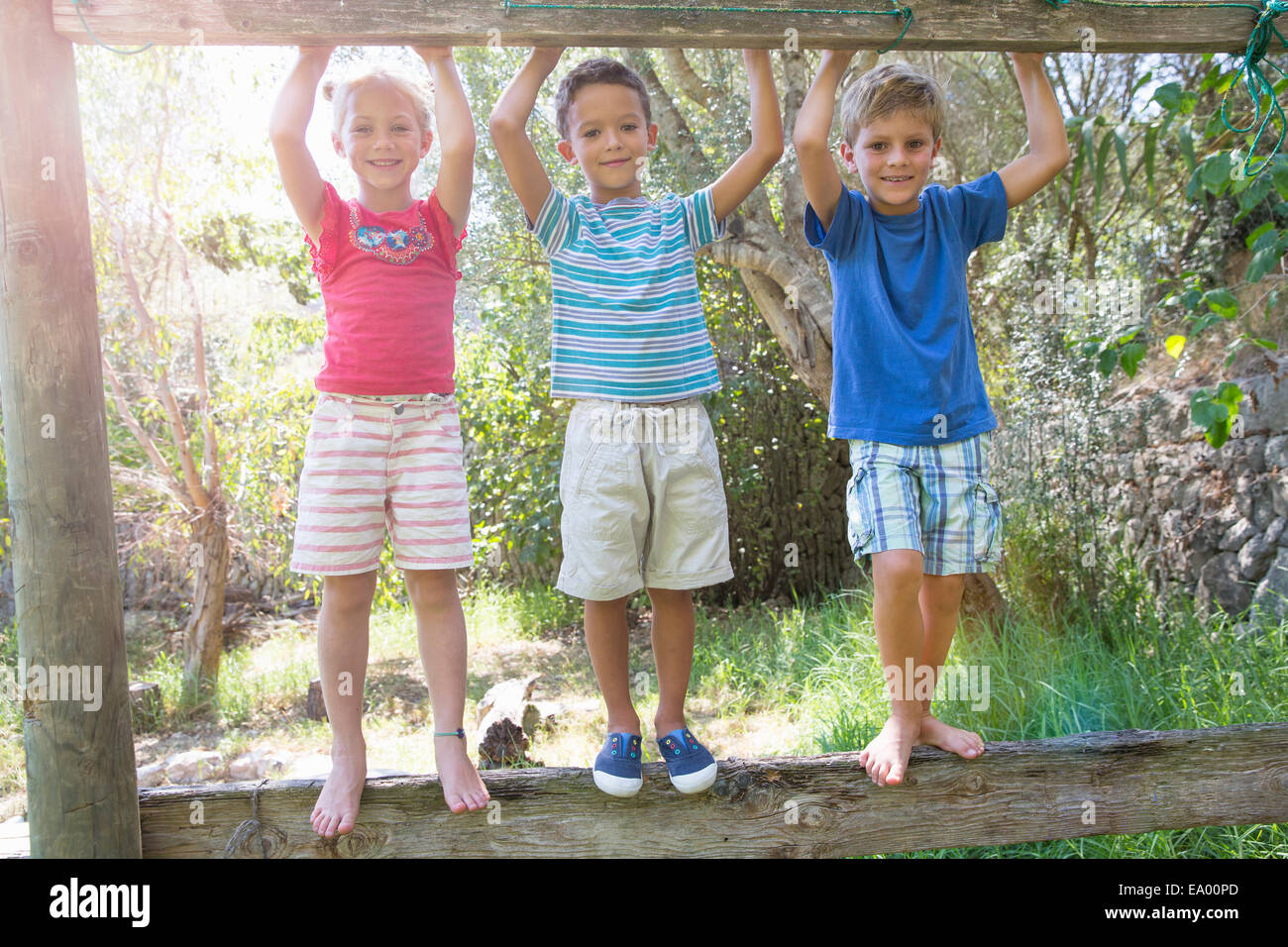 Three children in garden standing on fence Stock Photo