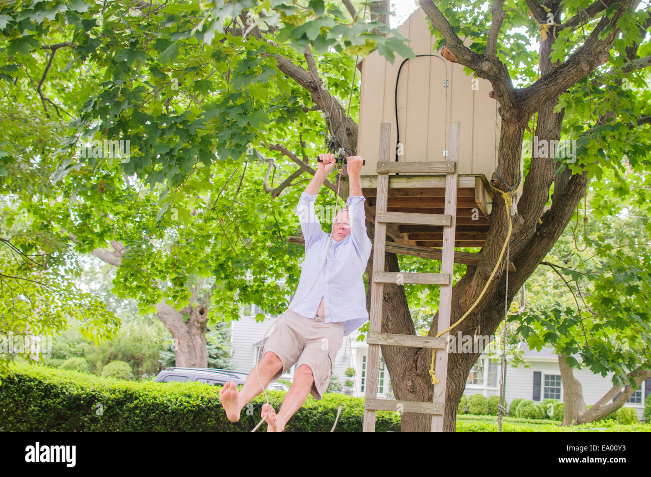 Mature man sliding down on pulley from tree house Stock Photo