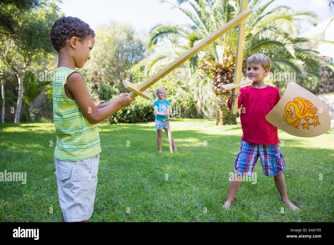 Three children in garden playing with toy swords Stock Photo