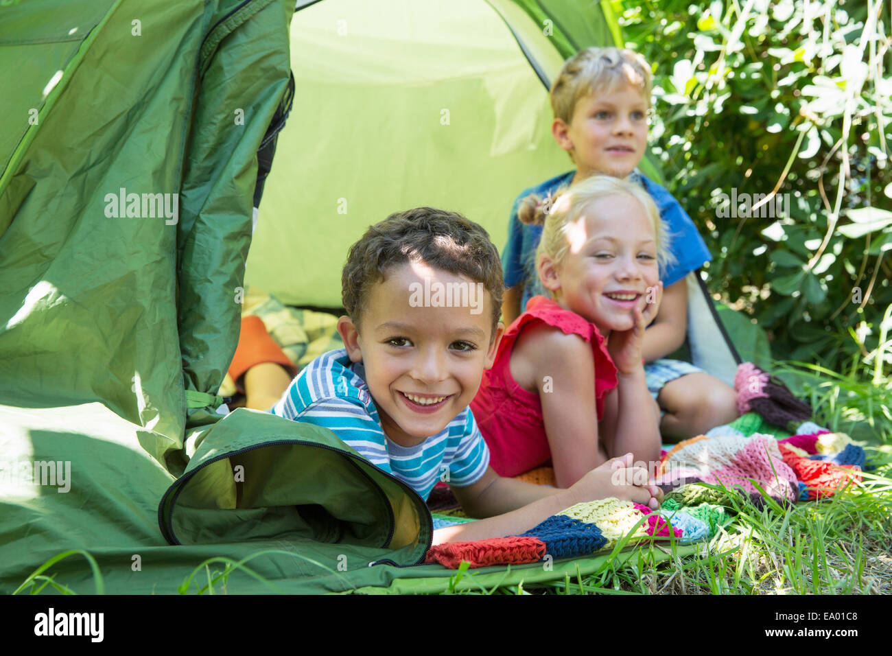 Portrait of three smiling children lying in garden tent Stock Photo