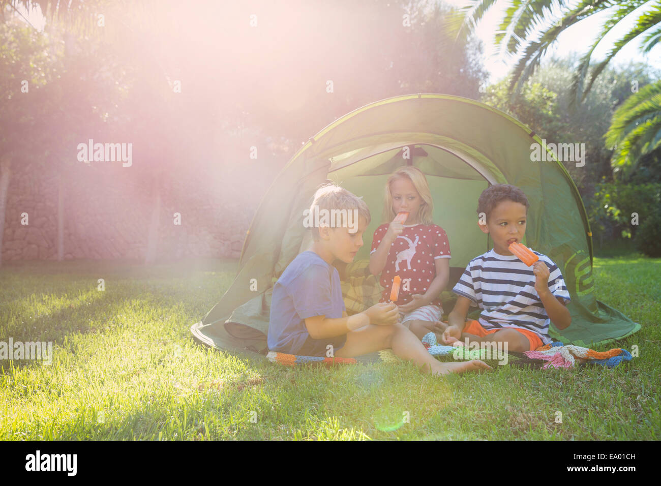 Three children eating ice lollies in garden tent Stock Photo