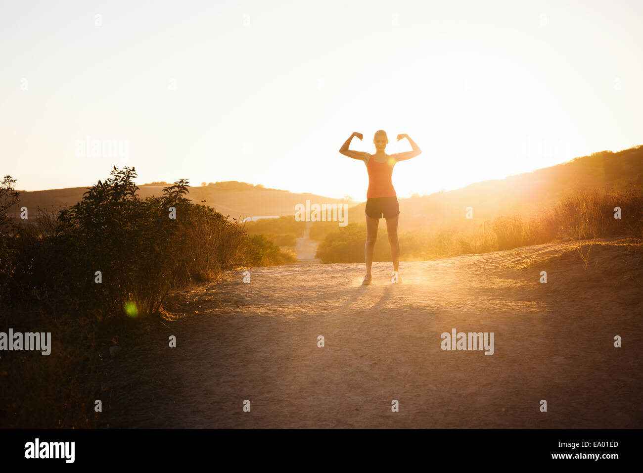 Female jogger flexing arms in sunlight, Poway, CA, USA Stock Photo