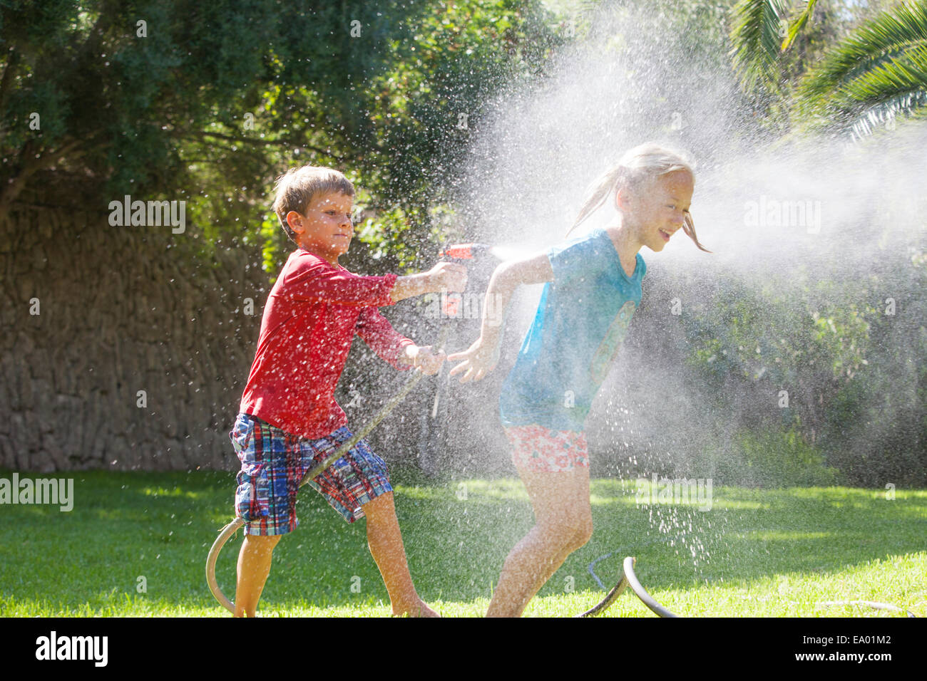 Boy splashing girl in garden with water sprinkler Stock Photo