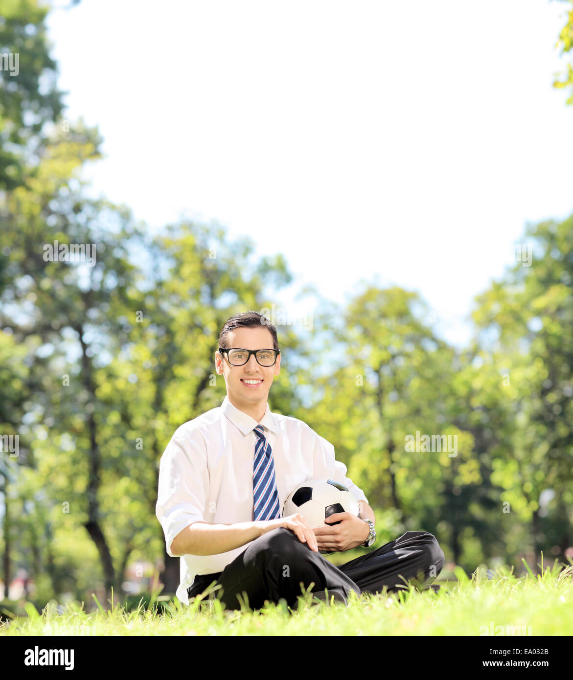 Young guy holding a football in park seated on the grass shot with a tilt ad shift lens Stock Photo