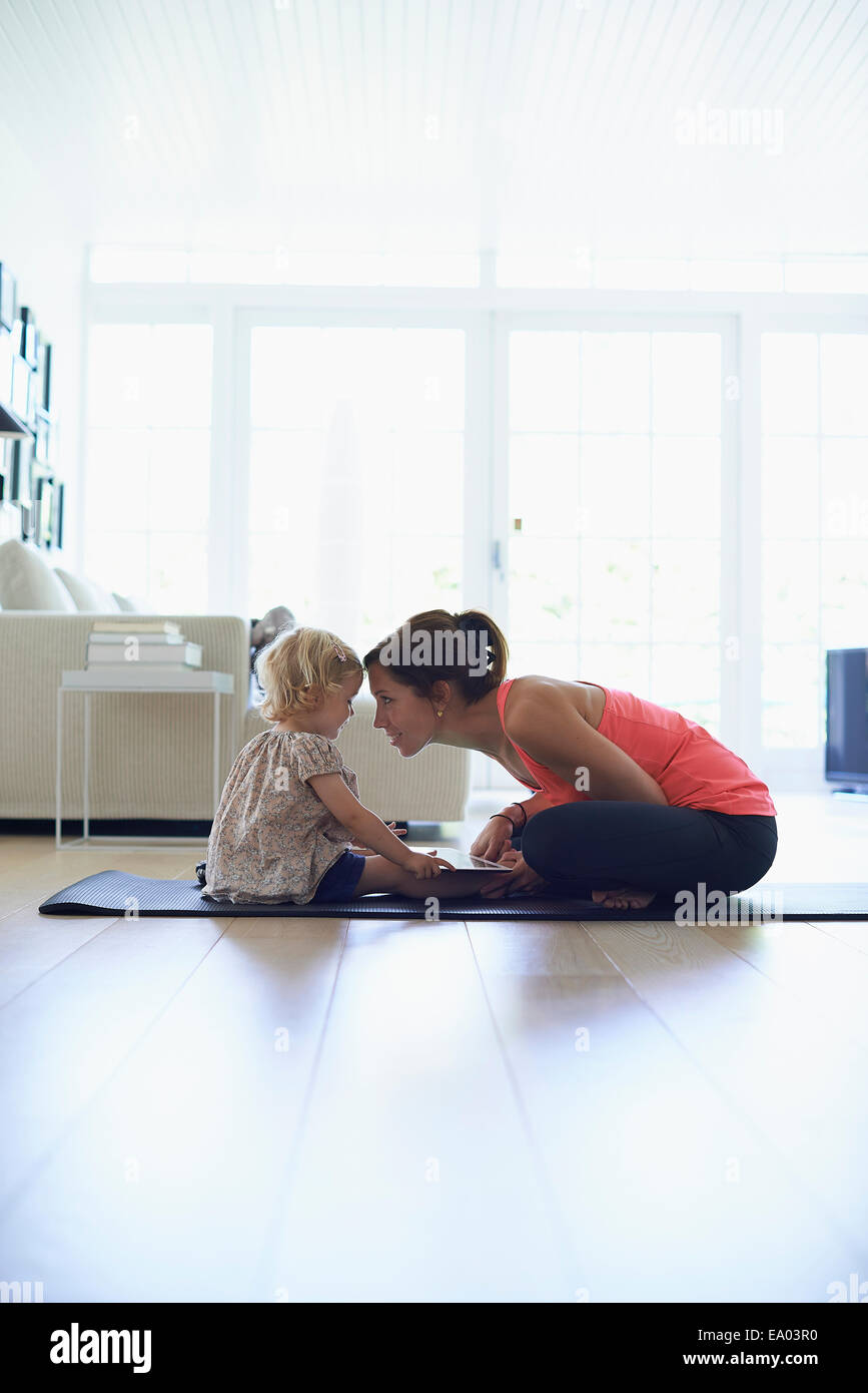 Mid adult mother and toddler daughter practicing lotus position in living room Stock Photo