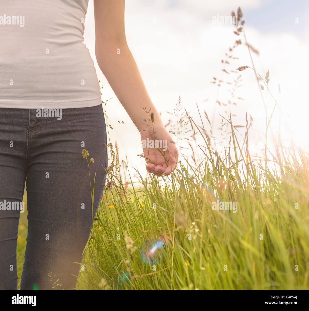 Young woman running hand through long grass in meadow under bright