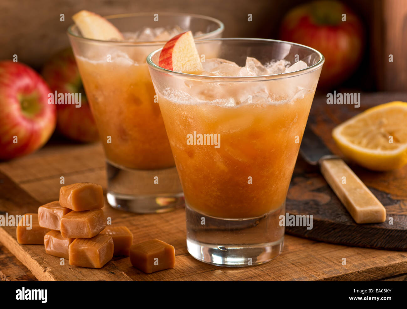 Caramel Apple Cider Cocktails on a rustic background with apples, caramels, and lemon. Stock Photo