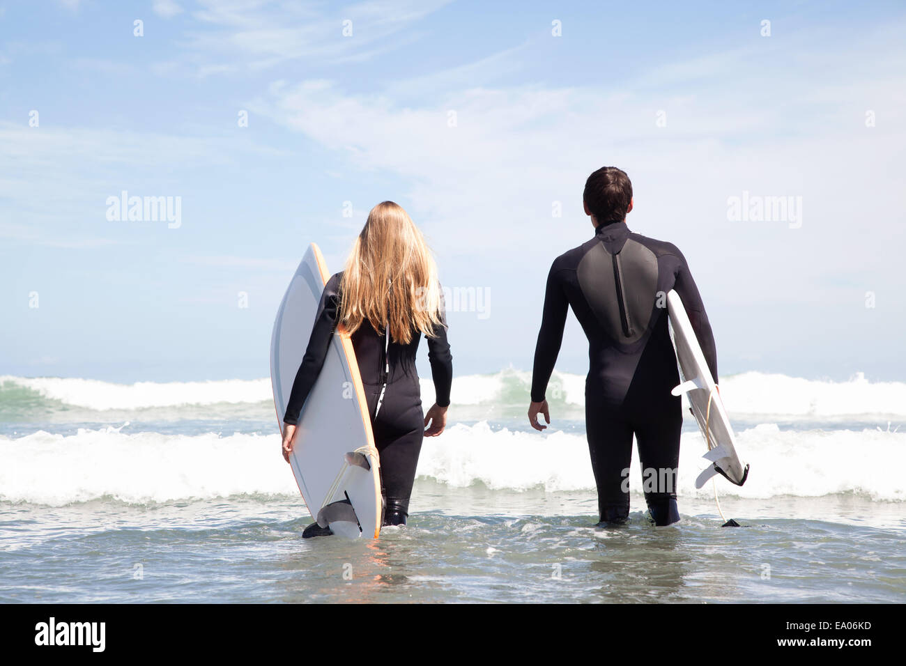 Young couple walking out to sea holding surfboards, rear view Stock Photo