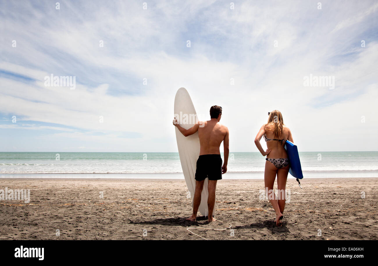 Young couple standing on beach holding surfboard and boogie board Stock Photo